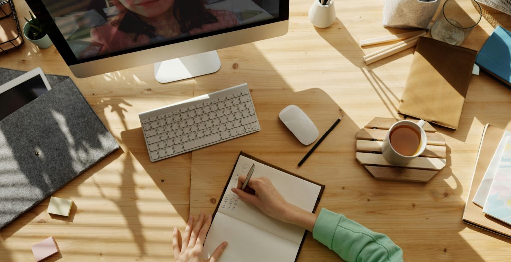 A student taking notes during a video call for online learning at home.